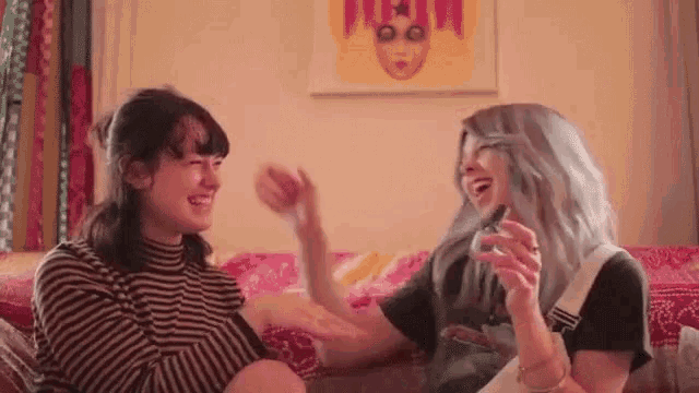 two women are sitting on a couch laughing and having fun .