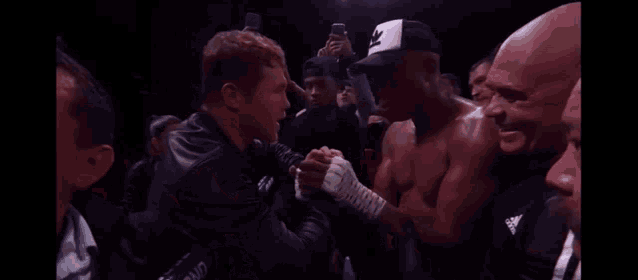 two men are shaking hands in a boxing ring while a crowd looks on .