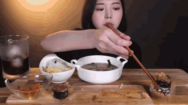 a woman is eating a bowl of soup with chopsticks while sitting at a table