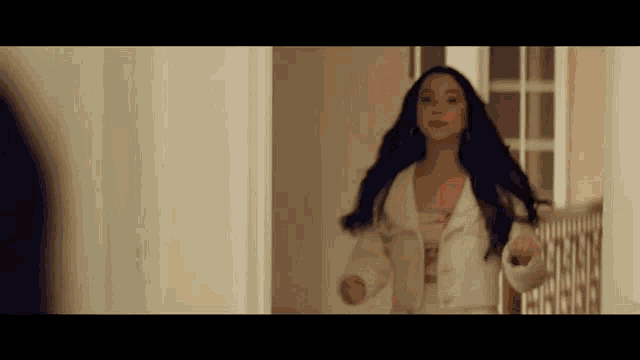 a woman in a white jacket is standing in a hallway and looking at herself in the mirror .