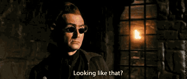a man wearing sunglasses is standing in front of a window in a dark room and looking like that .