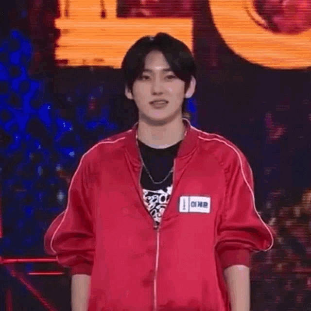 a young man in a red jacket is standing on a stage holding a microphone and smiling .
