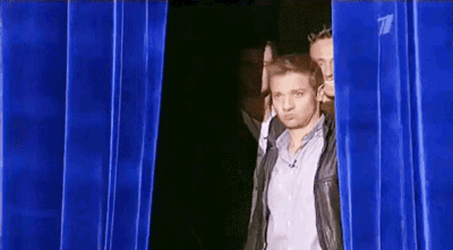 a man is standing in front of a blue curtain .