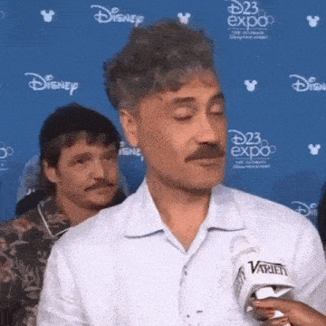 a man with a mustache is talking into a microphone at a convention .