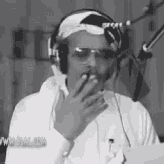 a man wearing headphones and sunglasses is smoking a cigarette in front of a microphone in a black and white photo .