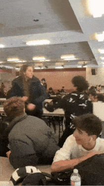 a group of people are sitting at tables in a room with a bottle of water in the foreground