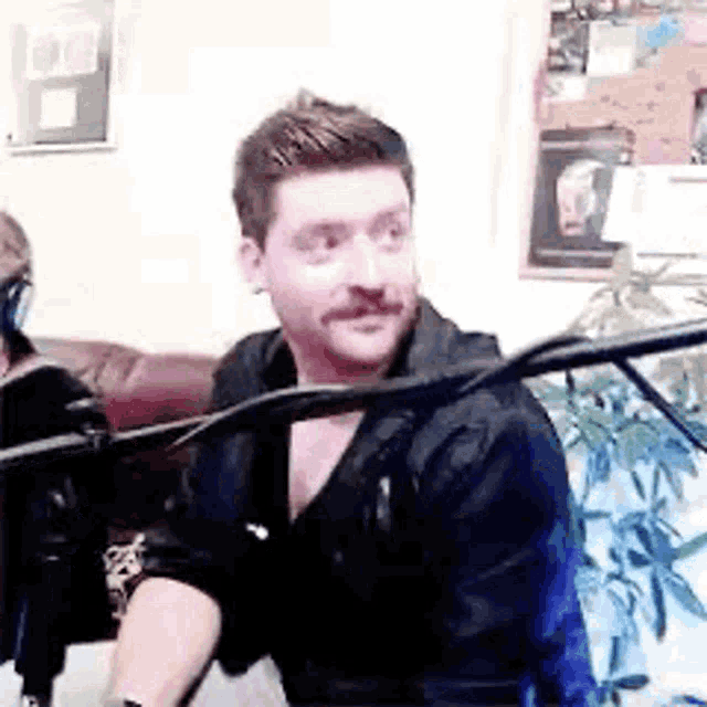 a man with a mustache is sitting in front of a microphone .