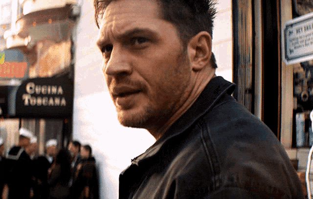 a man in a leather jacket stands in front of a sign that says cucina toscana