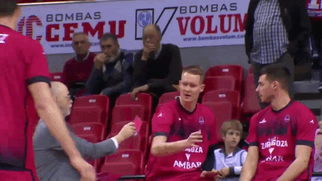 a man giving a red card to a basketball player in front of an advertisement for bombas volum