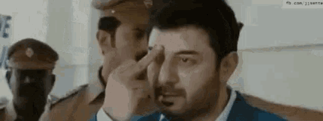 a man is covering his face with his hand while a man in a police uniform looks on .