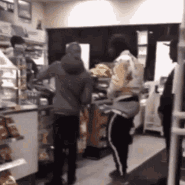 a group of people are standing in a bakery and talking to each other .