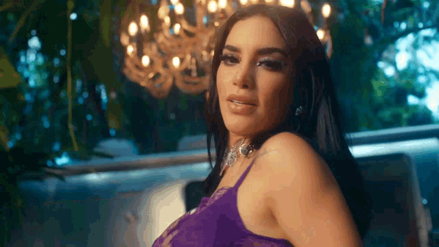 a woman in a purple bra looks at the camera with a chandelier in the background