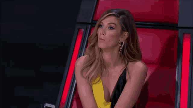 a woman in a yellow and black dress is sitting in a red chair and making a funny face .