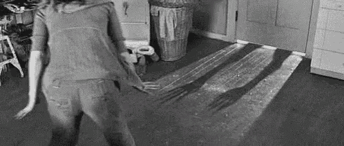 a black and white photo of a woman dancing in a kitchen with a fork shadow on the floor .