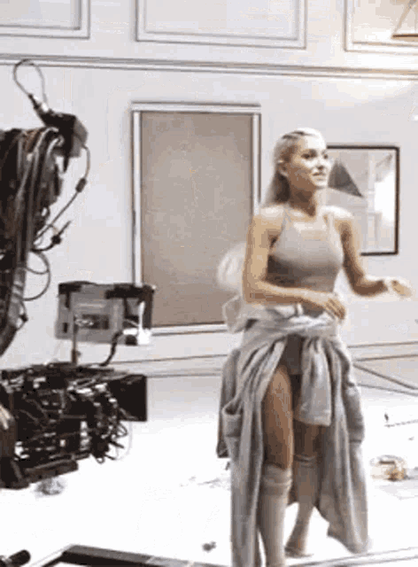 ariana grande is standing in front of a camera in a room with a camera .