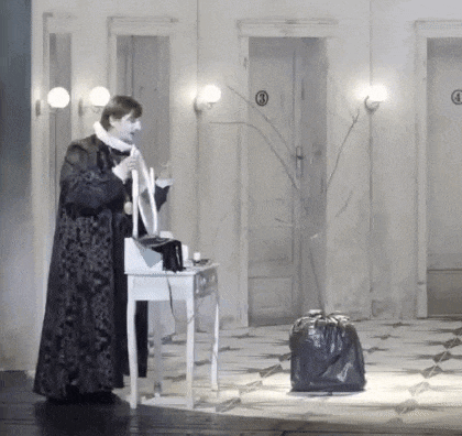 a man in a long coat is standing in front of a dressing table holding a microphone .