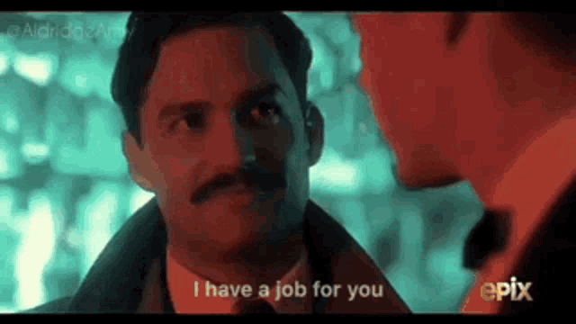 a man with a mustache is talking to another man in a dark room .
