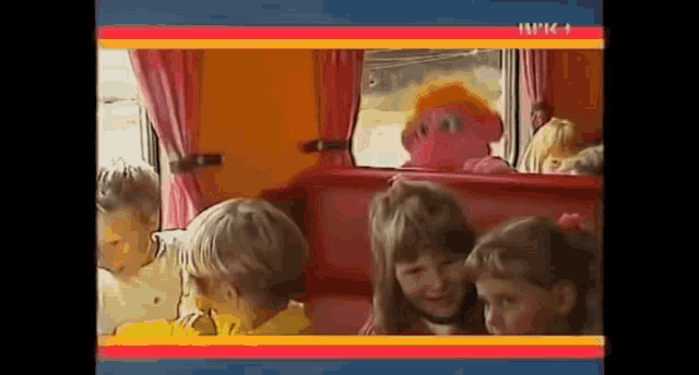 a group of children are sitting on a bus with a stuffed animal in the background .