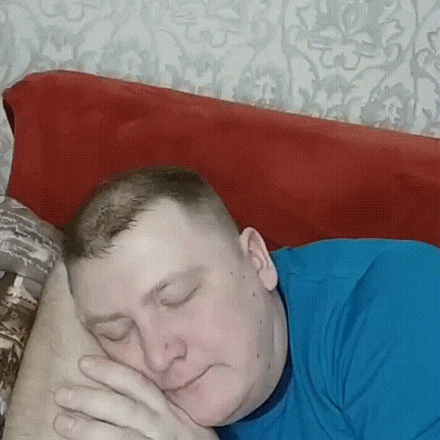 a man in a blue shirt sleeping on a bed