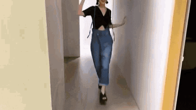 a woman is walking down a hallway wearing overalls and a crop top .