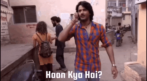 a man in a plaid shirt is talking on a cell phone in a narrow alleyway .
