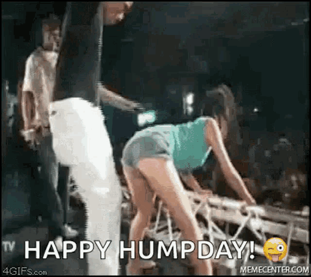 a man is standing next to a woman in shorts on a stage and says `` happy hump day ! ''