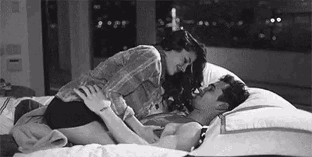 a black and white photo of a man and a woman kissing on a bed .