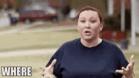 a woman in a blue shirt is standing in front of a house with her hands outstretched .