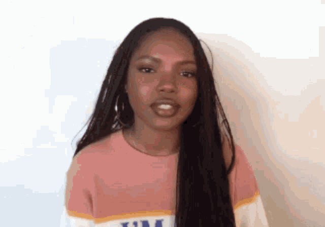 a woman with long braided hair is wearing a pink sweater and earrings .