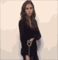 a woman in a black dress is standing with her arms crossed and holding an umbrella .