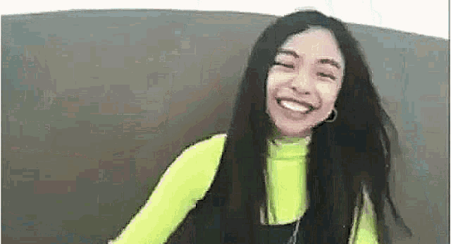 a woman is sitting on a couch smiling and wearing a neon green shirt .