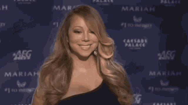 a woman in a black dress is standing in front of a wall with the word mariah on it