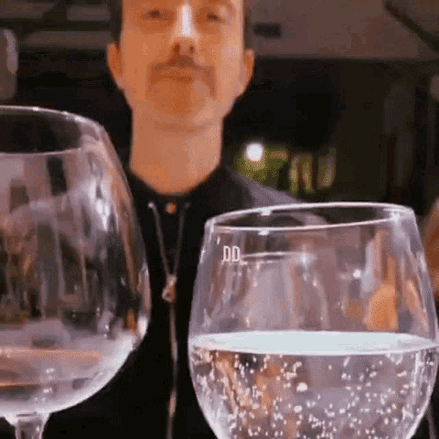a man with a mustache is standing next to two wine glasses .