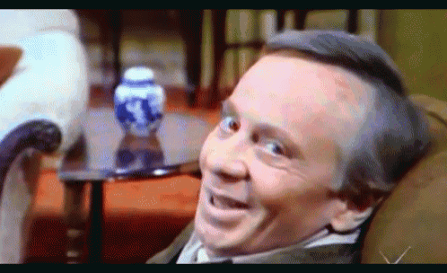 a man is sitting in a chair with a vase in the background