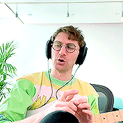 a man wearing headphones and a yellow and green shirt is playing a guitar