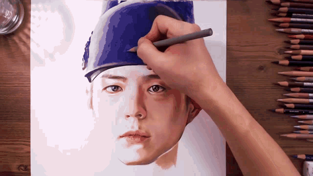 a person is drawing a portrait of a man wearing a blue hat with a pencil