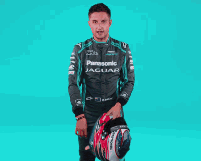 a man wearing a panasonic jaguar jacket is holding a helmet
