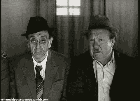 two men in suits and hats are sitting next to each other in a room and making funny faces .