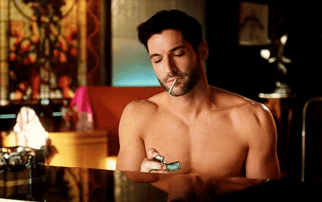 a shirtless man is smoking a cigarette in a dark room