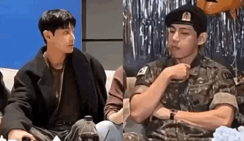 two men in military uniforms are sitting next to each other on a couch and talking to each other .
