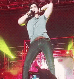 a man is singing into a microphone on a stage with a hand taking a picture