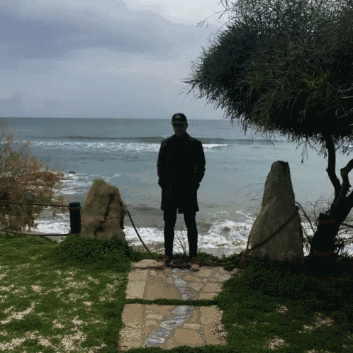 a man in a baseball cap stands in front of a body of water