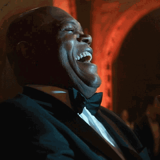 a man wearing a tuxedo and bow tie is laughing