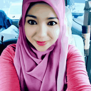 a woman wearing a pink hijab is taking a selfie in a car