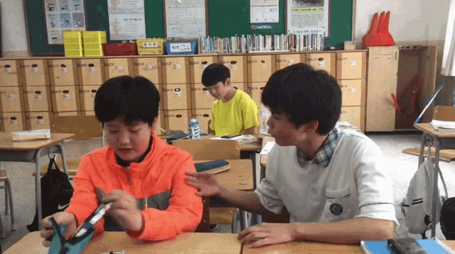 a boy in an orange jacket is talking to another boy in a yellow shirt