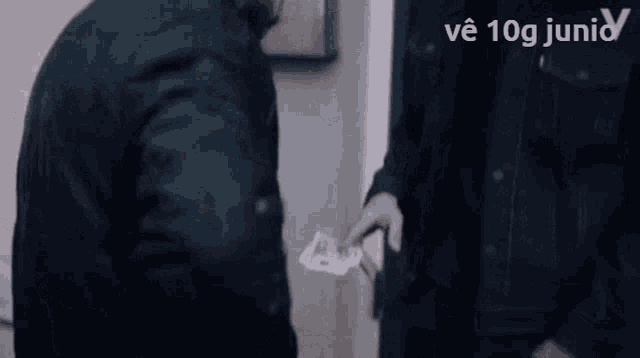 a man in a black jacket is handing another man a piece of paper