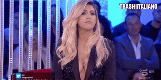 a woman in a very revealing jacket is sitting in front of a crowd and the words trash italiano are above her