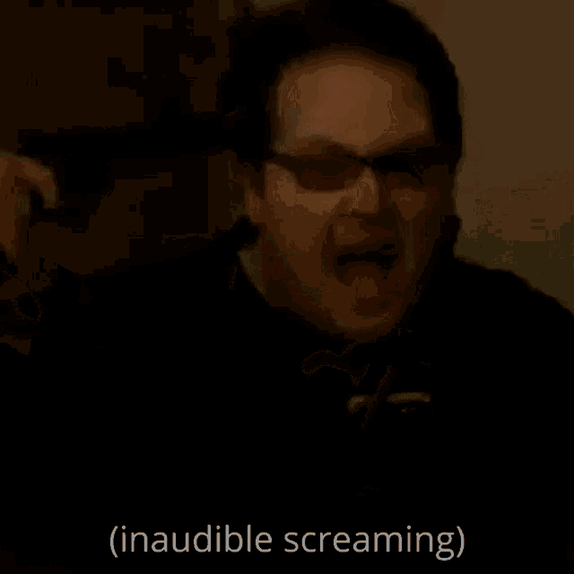 a man wearing glasses is screaming in a dark room with the words `` inaudible screaming '' written below him .