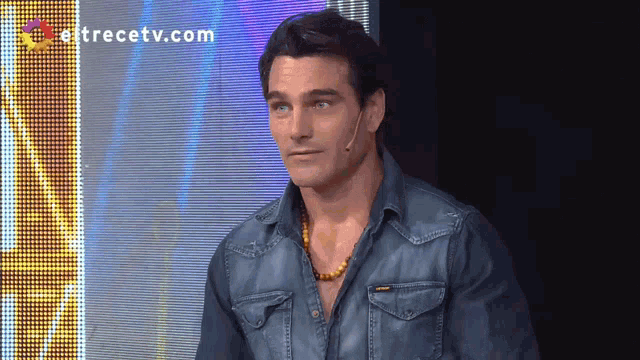a man in a denim shirt stands in front of a screen that says " entrectv.com "