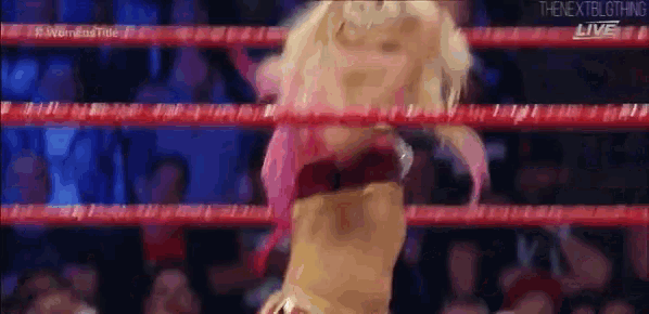a female wrestler is standing in a ring with a crowd watching .